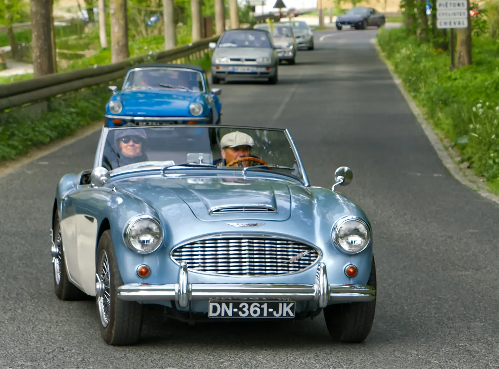 A light blue vintage convertible on a country road
